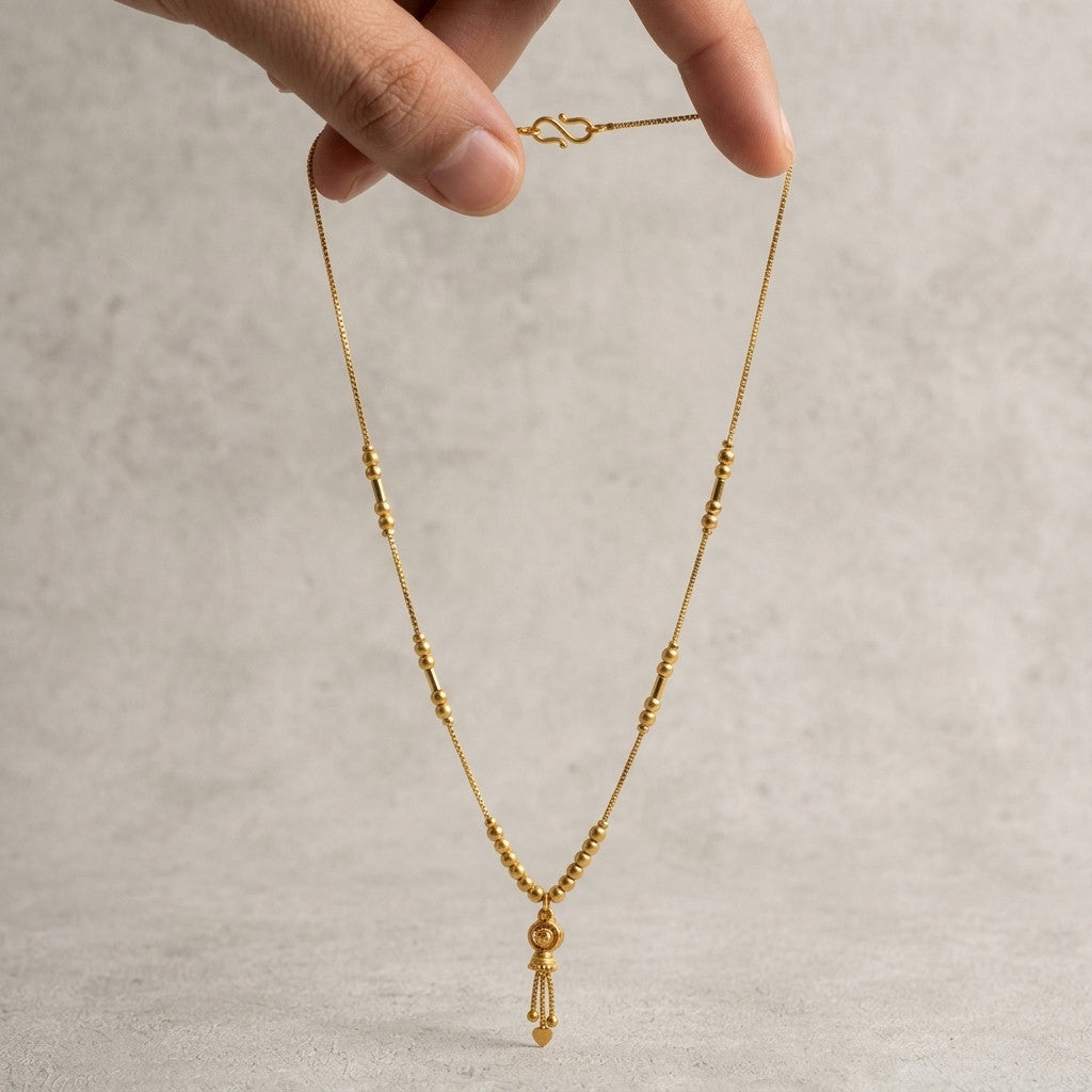Hand holding delicate gold-tone beaded necklace with heart pendant