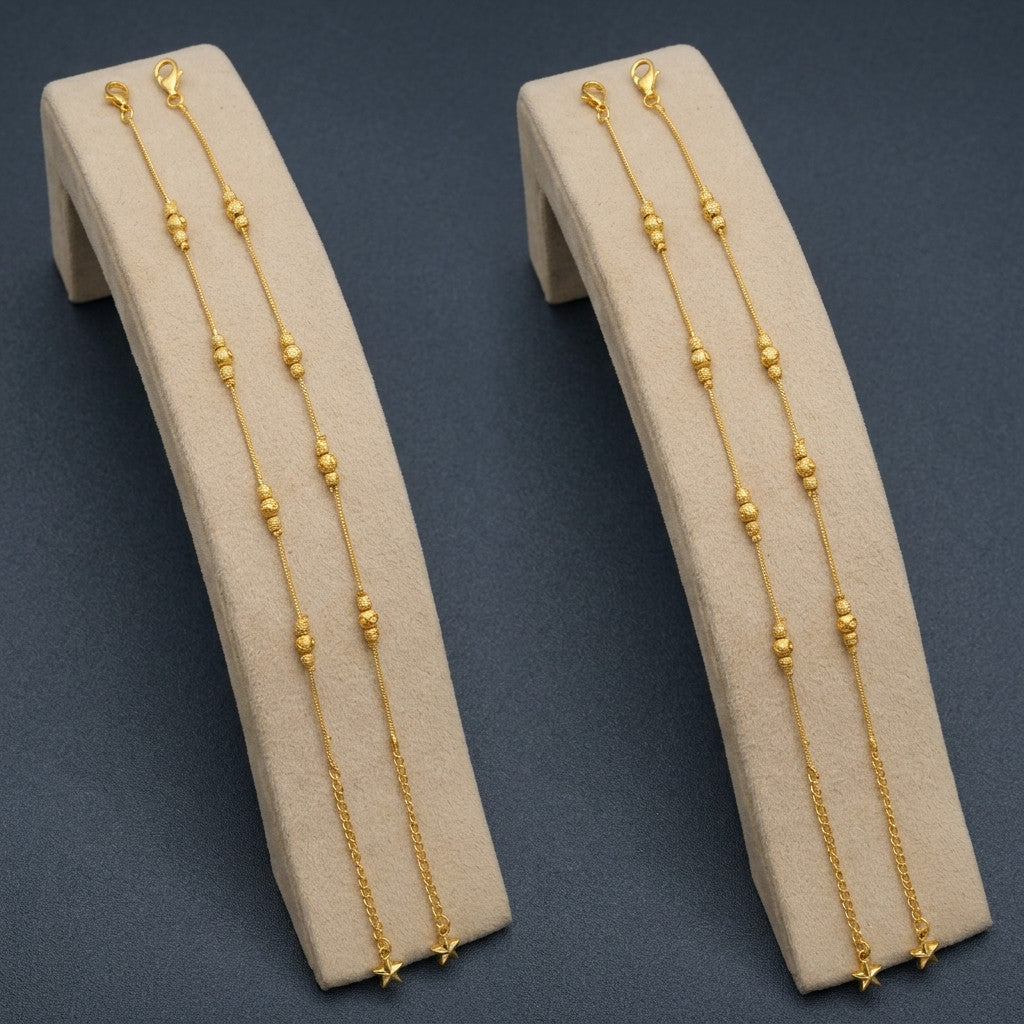Two gold-tone beaded anklets displayed on beige stand