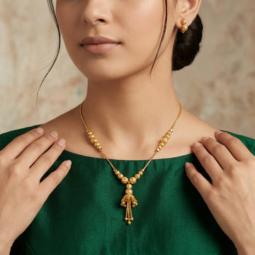 Model wearing gold-tone beaded tassel necklace with matching earrings