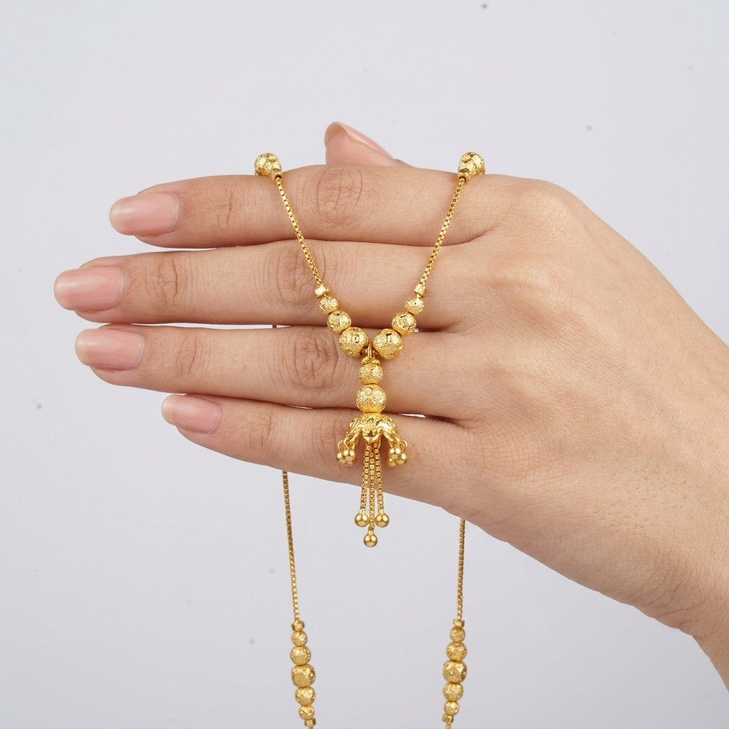 Gold-tone necklace held in hand showcasing beaded details and tassel pendant