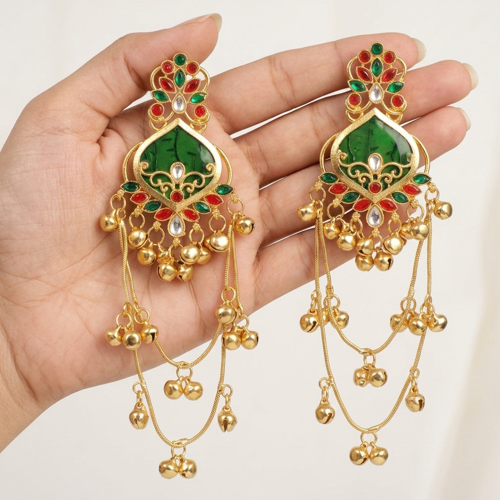 Close-up of gold-tone drop earrings with green and red stone-look details held in hand