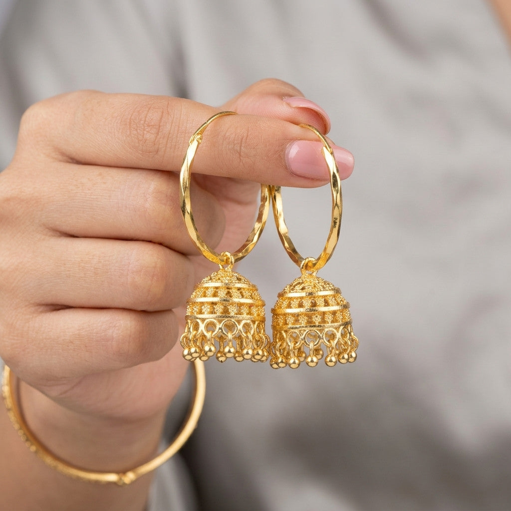 Hand holding pair of gold-tone hoop earrings with intricate jhumka pendants