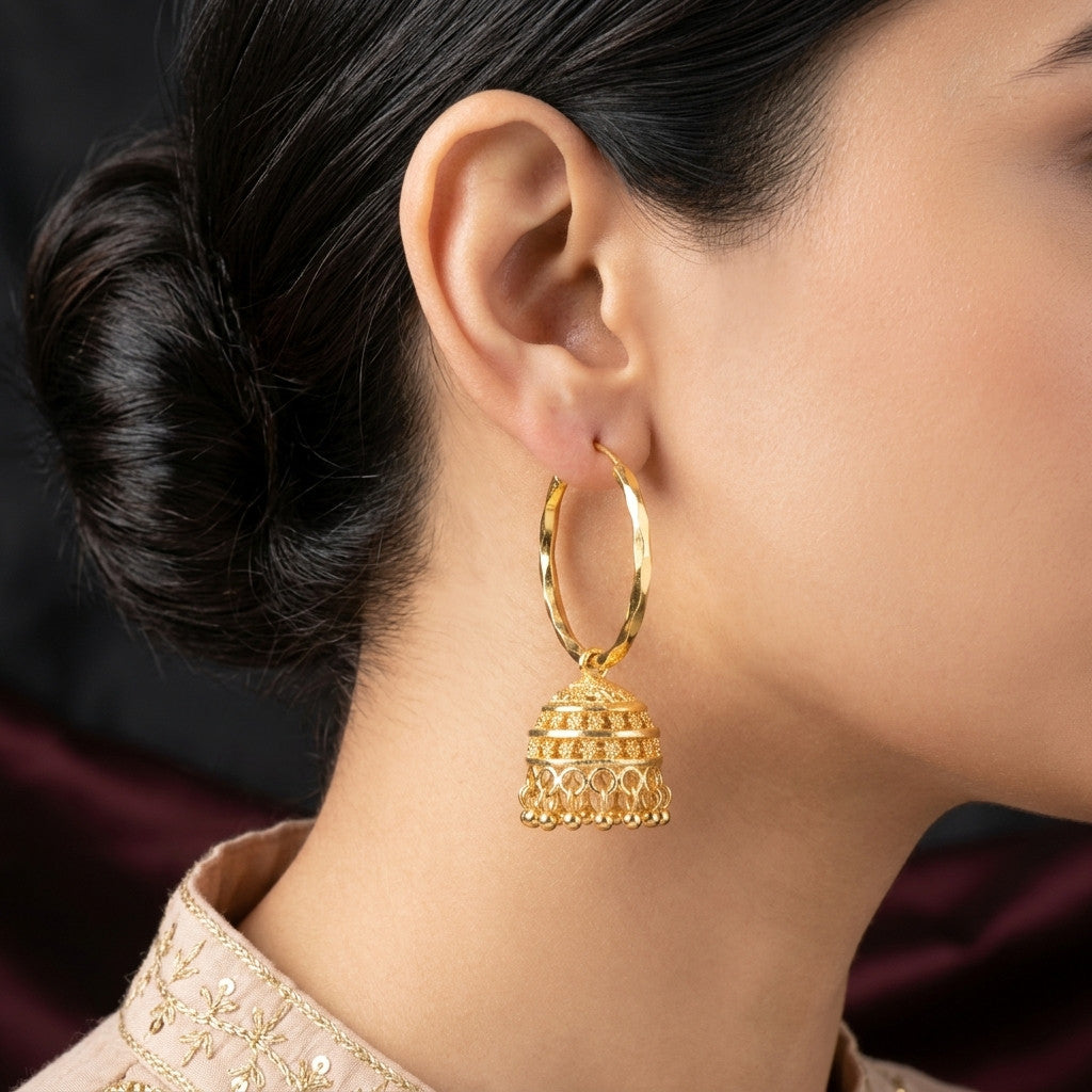 Close-up of model wearing gold-tone jhumka hoop earring with dark background