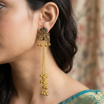 Model wearing gold-tone long chain bell drop earring with green and red accents