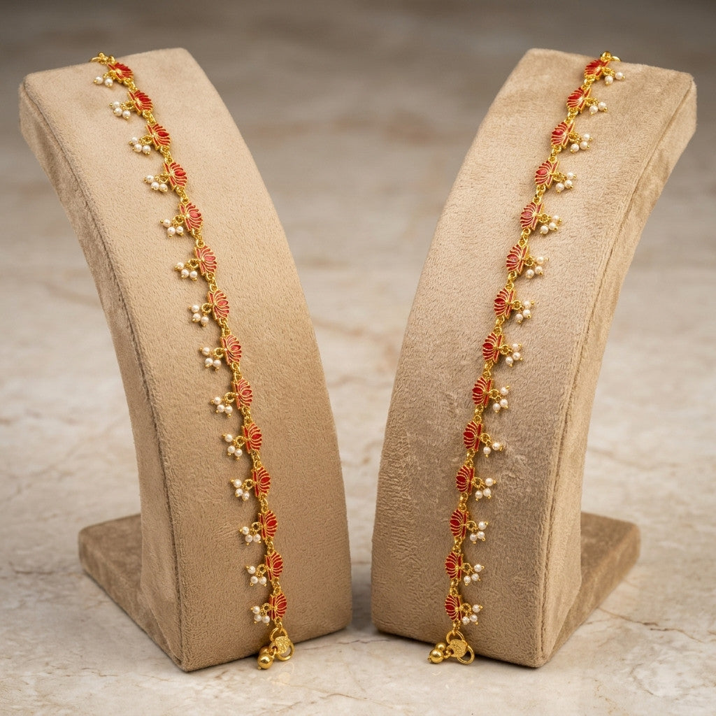 Two gold-tone lotus motif anklets with red enamel and pearl-look beads on beige display stands