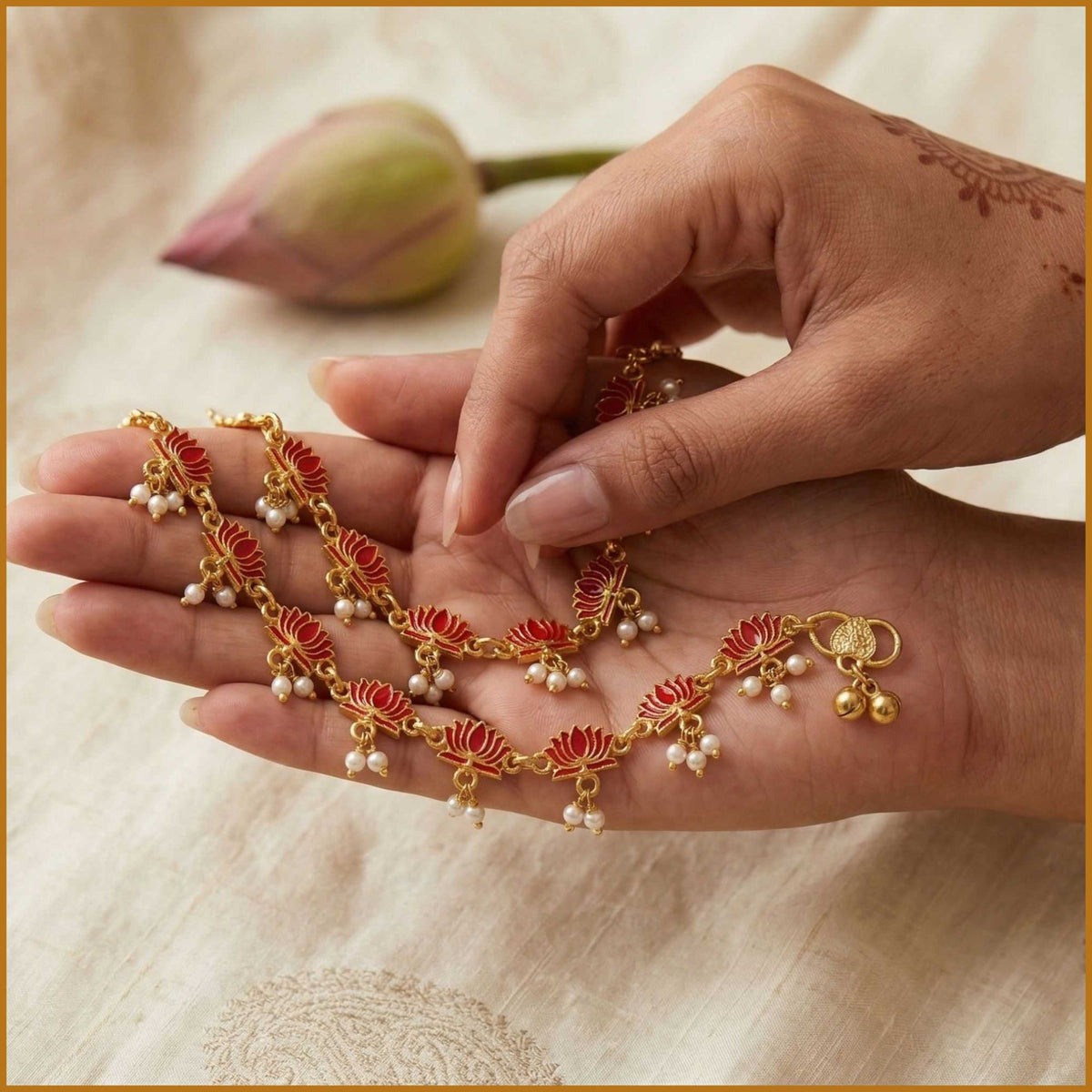Hand holding gold-tone lotus motif anklet with red enamel and pearl-look bead dangles