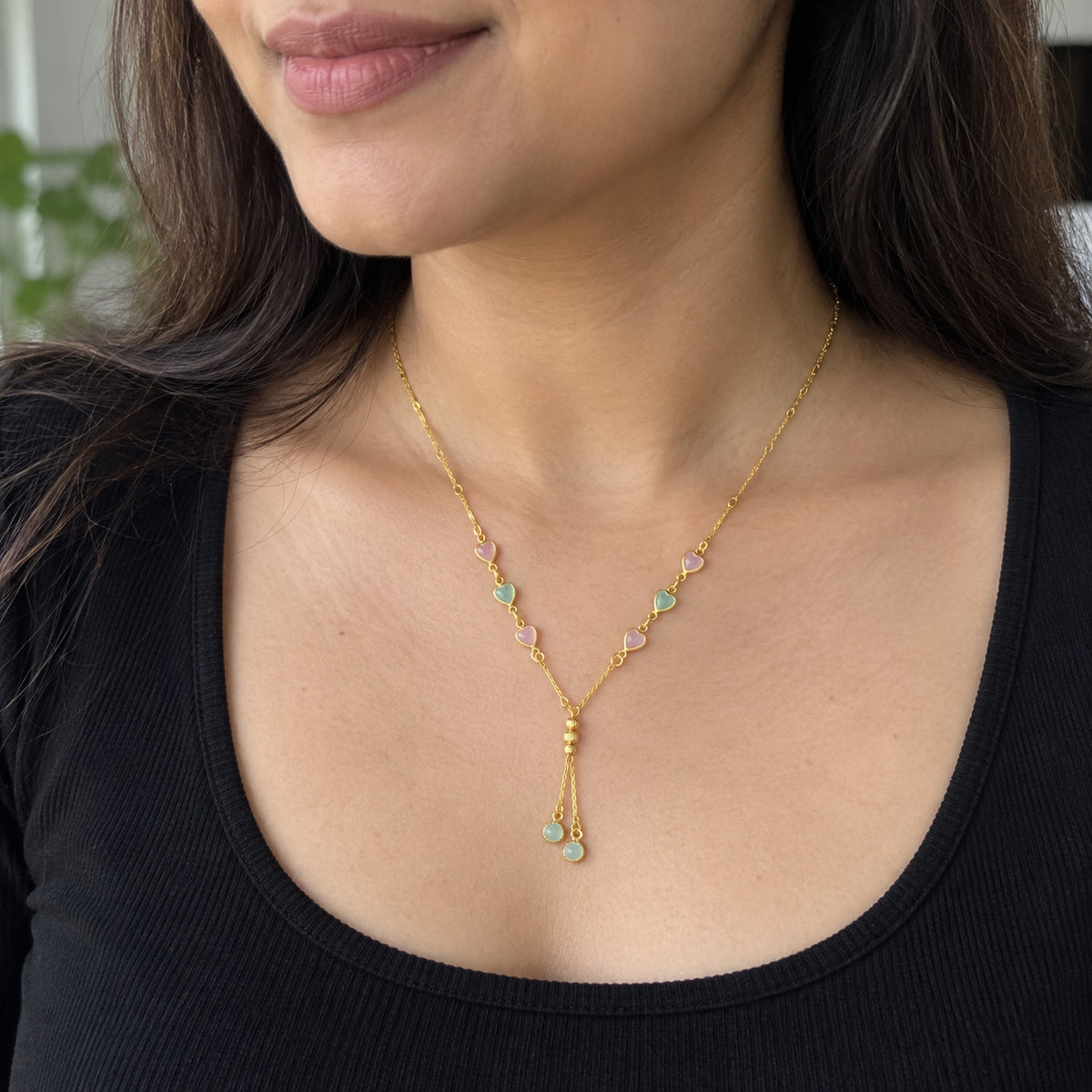 Close-up of gold-tone necklace with pink and green heart accents worn