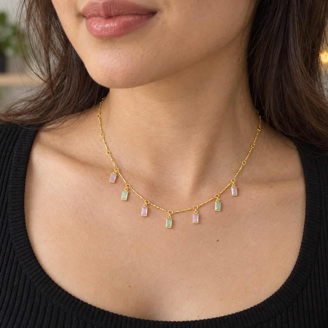 Woman wearing necklace with gold-tone chain and pastel rectangular charms alternating pink and green