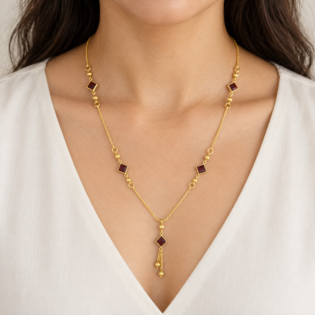 Gold-tone necklace with red square stone-look accents worn on model