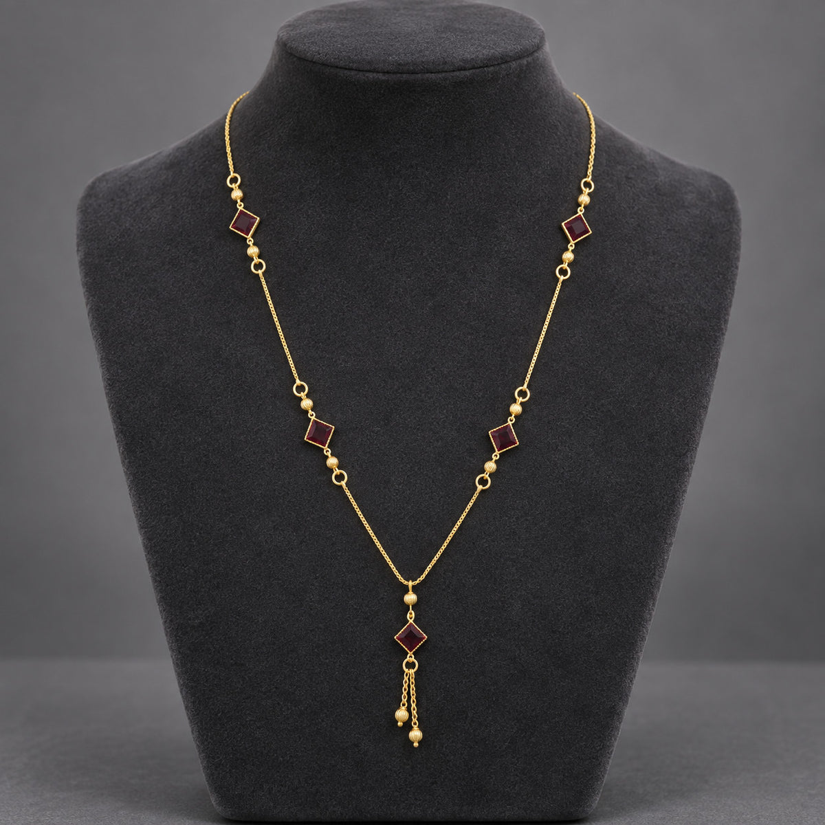 Front view of gold-tone necklace with red stone-look accents on display bust