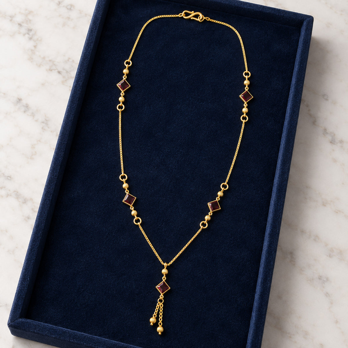 Gold-tone necklace with red stone-look accents laid in blue velvet box