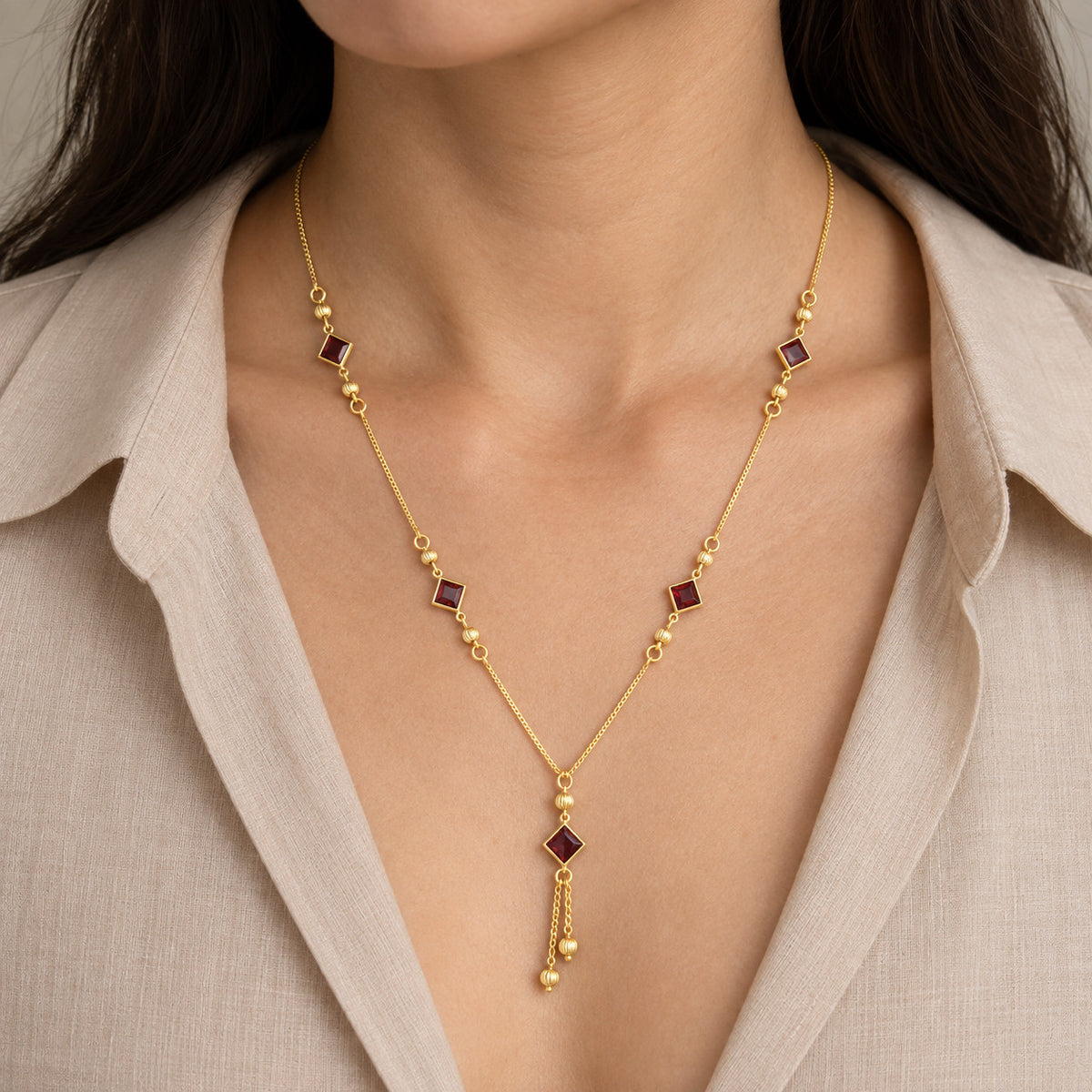 Model wearing gold-tone necklace with red stone-look square charms and pendant tassel