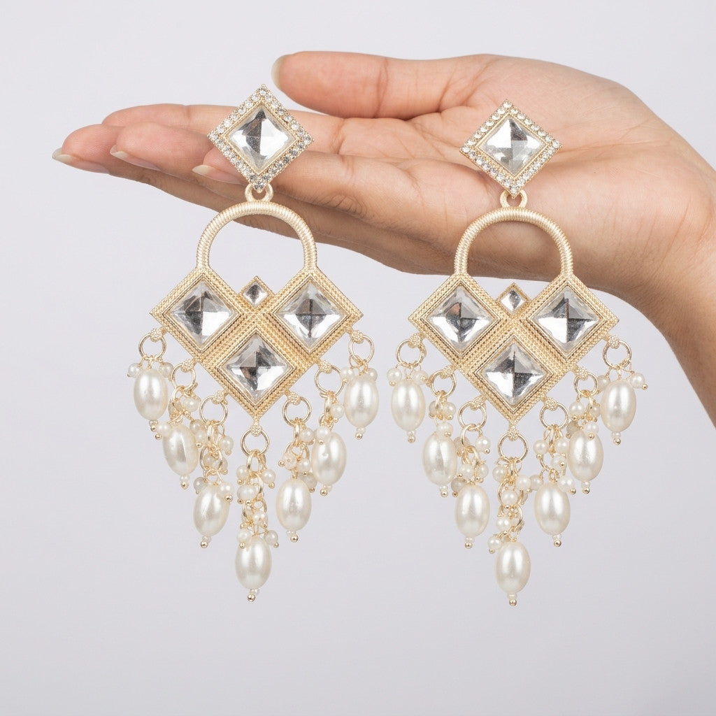 Gold-tone dangle earring with clear square stones and pearl-look beads worn on ear