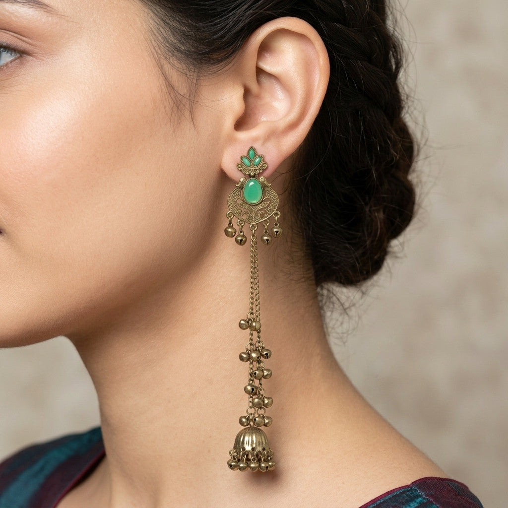 Model wearing long antique gold-tone earrings with green stones and dangling chains