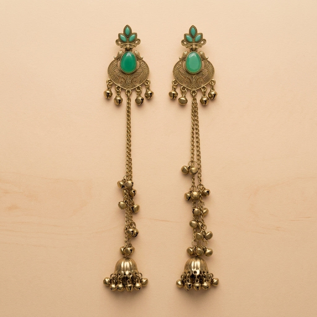 Pair of long antique gold-tone earrings with green stone accents on beige background