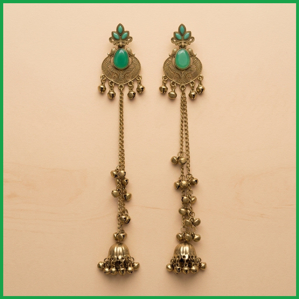 Close-up of long antique gold-tone earrings with green stones and hanging bell ornaments