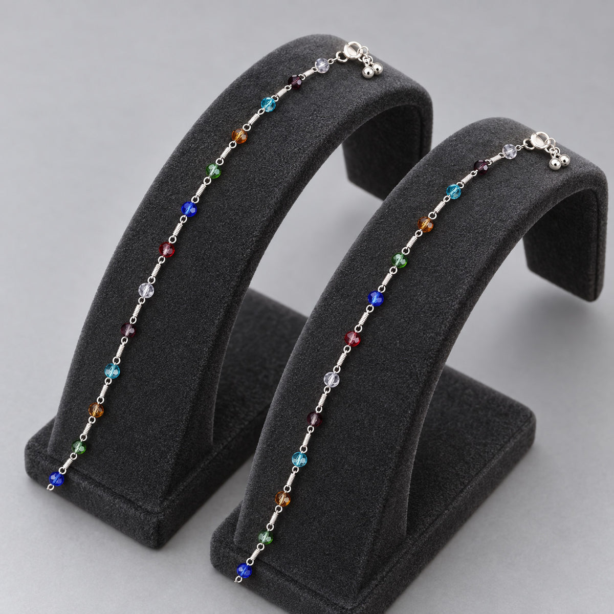 Pair of multicolour beaded anklets displayed on grey stands