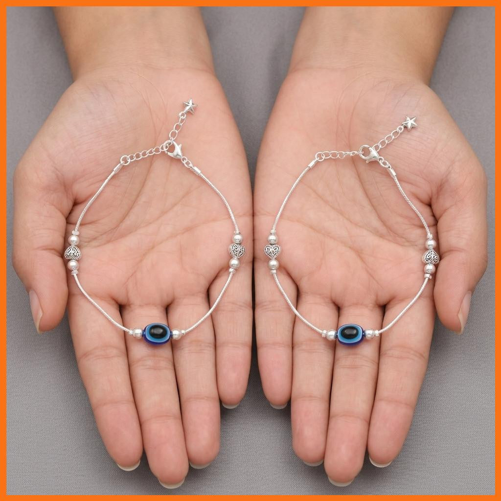 Close up of both anklets held in hands showing blue and black oval bead and decorative silver-tone elements