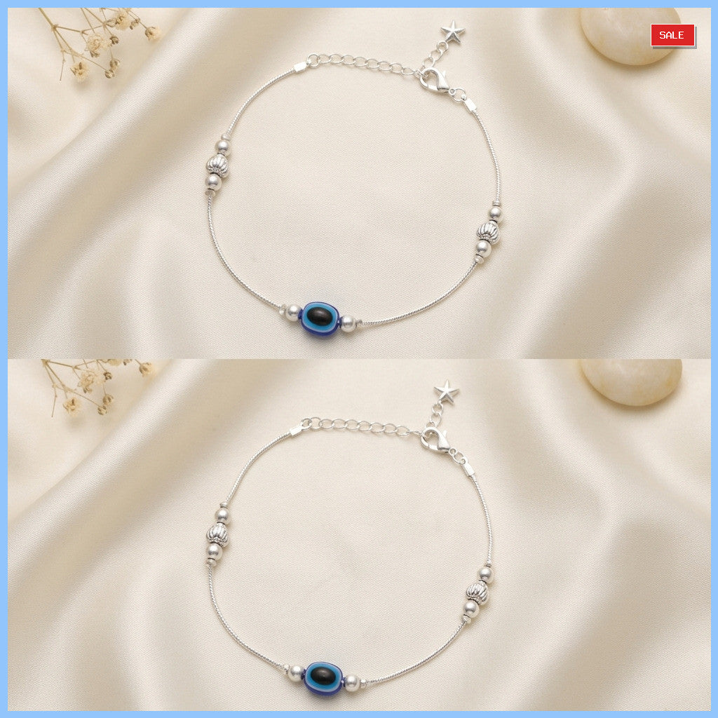 Silver-tone anklet displayed on cream fabric background with blue and black bead and star charm