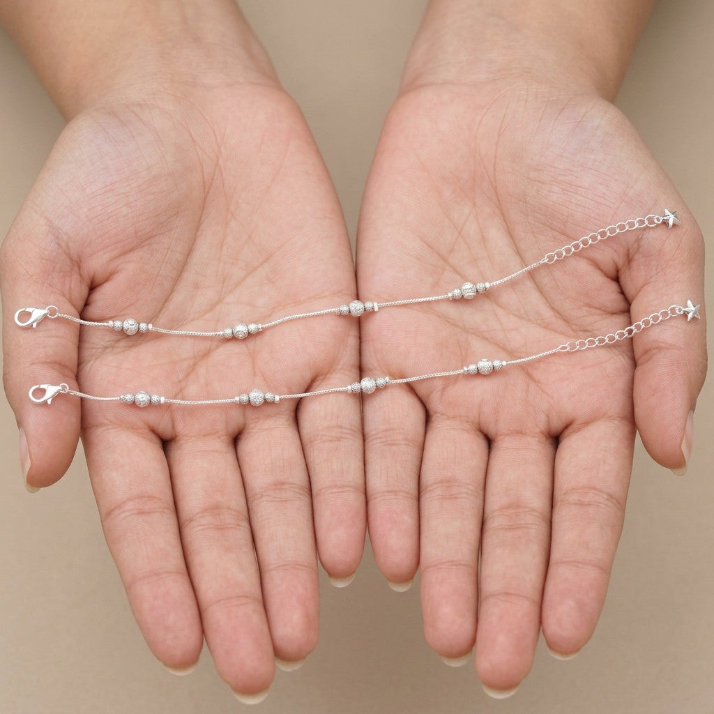 Two silver-tone beaded anklets held in hands to display design and clasp