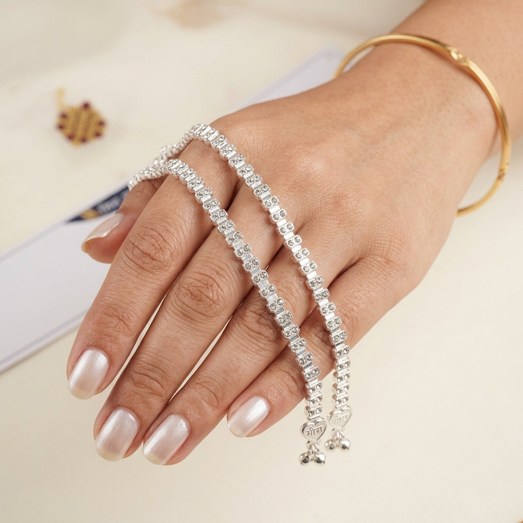 Two silver-tone anklets displayed on hand with clear crystal embellishments
