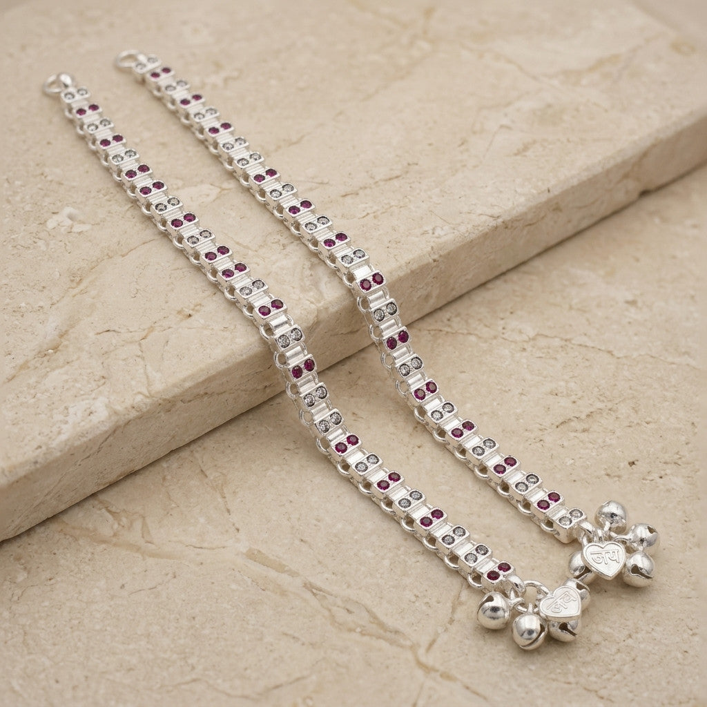 Pair of silver-tone dual-row red and clear stone-look anklets displayed on stone surface