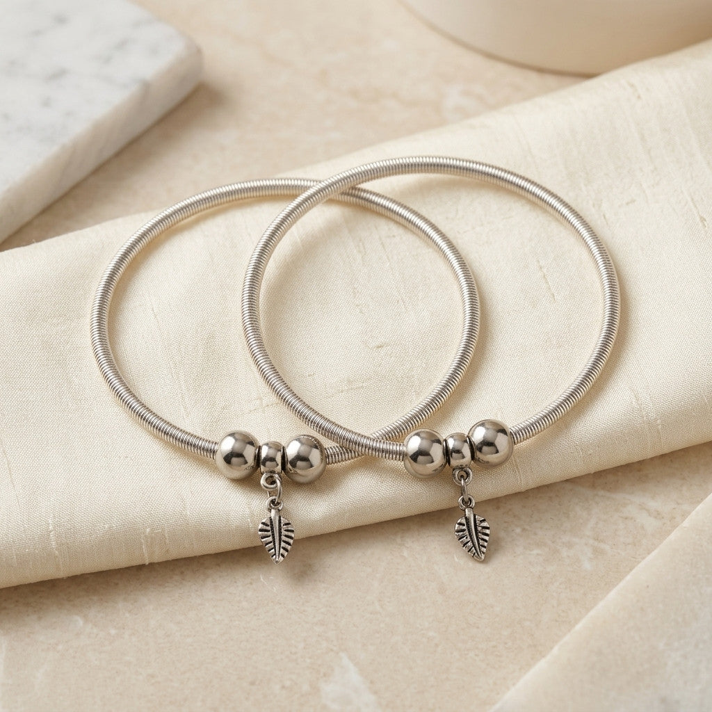 pair of silver-tone leaf charm anklets on fabric