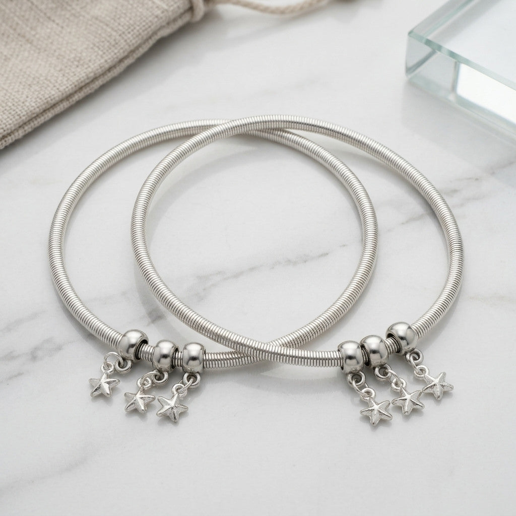 Two silver-tone snake chain anklets with star-shaped charms displayed on white surface