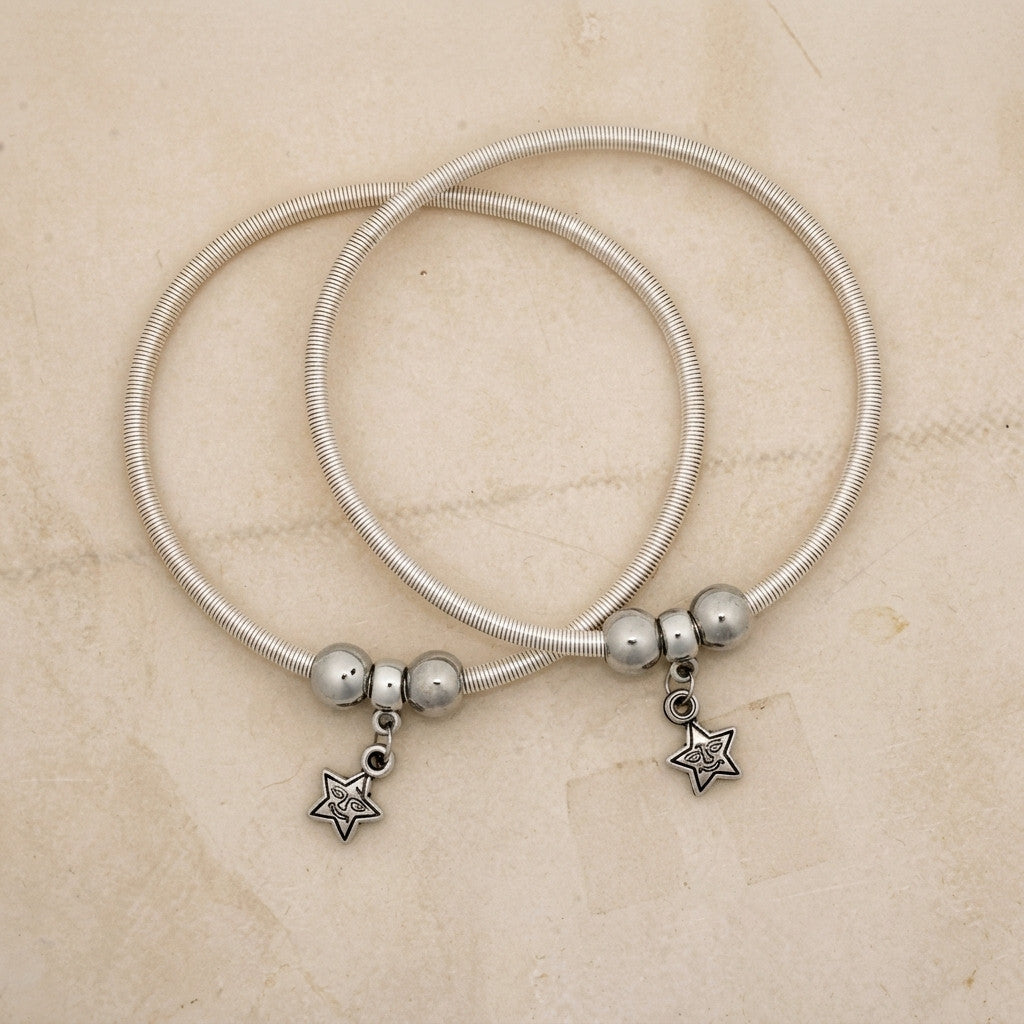 Two silver-tone star charm anklets displayed on a beige surface